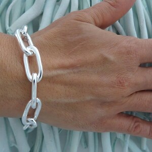 May include: A silver chain bracelet with large, oval-shaped links. The bracelet is worn on a person's wrist.