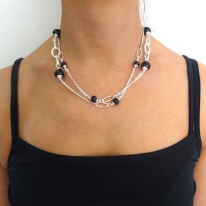 May include: A silver chain necklace with black beads. The necklace is layered and has a delicate design.