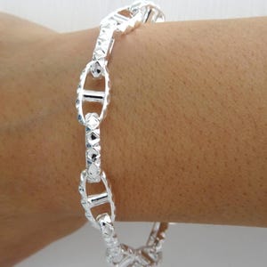 May include: A silver bracelet with a textured, mariner link chain design.