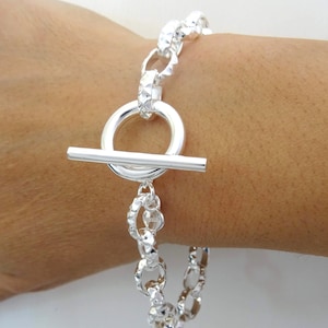 May include: A silver bracelet with a toggle clasp and a textured chain design.