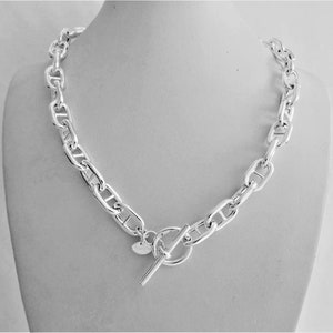 Può includere: Una collana a catena d'argento con chiusura a scatto. La catena è composta da maglie ovali spesse.