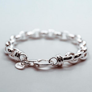 Könnte beinhalten: Ein silbernes Kettenarmband mit einem dicken, gedrehten Gliederdesign. Das Armband hat einen Verschluss und ein kleines silbernes Schild mit der Gravur "remarkable".