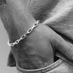 Peut inclure: Un bracelet en argent à maillons de chaîne. Le bracelet est composé de maillons rectangulaires et ovales. Le bracelet est porté au poignet. L'image est en noir et blanc.