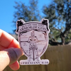 May include: A white sticker with a black outline depicting a knight in armor with a sword. The sticker has the text "Put on the full armor of God" and "Ephesians 6:10". The knight's armor is labeled with different parts of the armor of God, such as "helmet of salvation", "shield of faith", and "sword of the spirit".