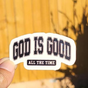 May include: White sticker with black text that reads "God is Good" in an arched font with the words "All the Time" underneath.