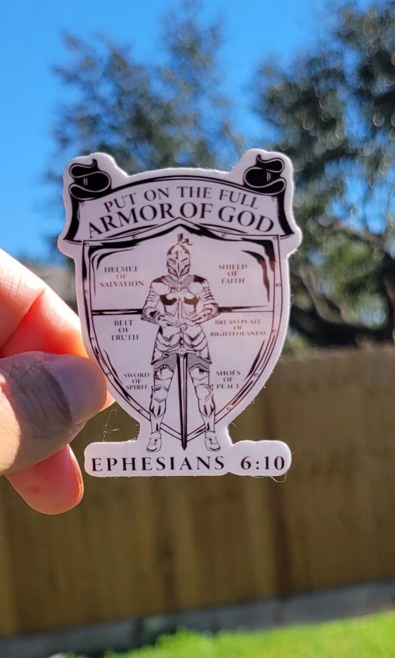 May include: A white sticker with a black outline of a knight in armor. The knight is holding a sword and is surrounded by a shield with the words "Put on the full armor of God" and "Ephesians 6:10". The shield is divided into sections with the names of the different pieces of armor: helmet of salvation, shield of faith, breastplate of righteousness, belt of truth, sword of the spirit, and shoes of peace.