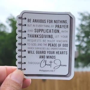 May include: White sticker with a black border and a spiral binding. The sticker features a quote from Philippians 4:6-7, "Be anxious for nothing, but in everything by prayer and supplication, with thanksgiving, let your requests be made known to God; and the peace of God, which surpasses all understanding, will guard your hearts and minds through Christ Jesus."