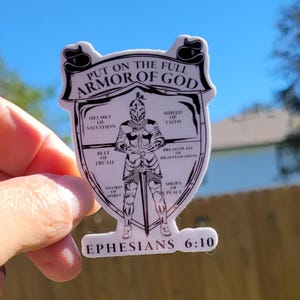 May include: A white sticker with a black and white illustration of a knight wearing armor. The text "PUT ON THE FULL ARMOR OF GOD" is at the top of the sticker. The text "EPHESIANS 6:10" is at the bottom of the sticker. The armor is labeled with different parts of the armor of God, such as "helmet of salvation", "shield of faith", "breastplate of righteousness", "belt of truth", "sword of the spirit", and "shoes of peace".