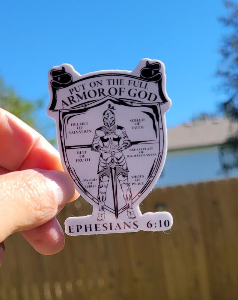 May include: A white sticker with a black and white illustration of a knight wearing armor. The text "PUT ON THE FULL ARMOR OF GOD" is at the top of the sticker. The text "EPHESIANS 6:10" is at the bottom of the sticker. The armor is labeled with different parts of the armor of God, such as "helmet of salvation", "shield of faith", "breastplate of righteousness", "belt of truth", "sword of the spirit", and "shoes of peace".