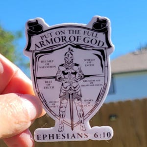 May include: A white sticker with a black and white illustration of a knight in armor. The text "PUT ON THE FULL ARMOR OF GOD" is at the top of the sticker. The text "EPHESIANS 6:10" is at the bottom of the sticker. The knight is wearing a helmet, shield, breastplate, belt, sword, and shoes. Each piece of armor is labeled with a corresponding part of the armor of God from the Bible verse Ephesians 6:10-18.