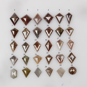 May include: Thirty loose diamonds, each with a unique shape and color, are arranged in rows on a white surface. The diamonds are mostly brown and gray, with some having a hint of green or yellow. The diamonds are all cut in a kite shape, with a pointed tip and a flat base.