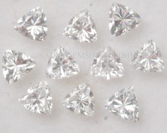 Pode incluir: Dez pedras preciosas triangulares transparentes, também conhecidas como diamantes de corte trilliant, são exibidas em uma superfície branca. As pedras preciosas são dispostas em um grupo solto.