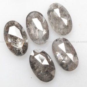Pode incluir: Cinco diamantes cinzentos de forma oval com corte facetado. Os diamantes est&atilde;o dispostos em semic&iacute;rculo sobre uma superf&iacute;cie branca.