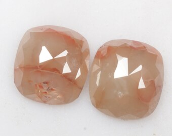 May include: Two light brown, faceted, cushion-shaped gemstones with a reddish hue.