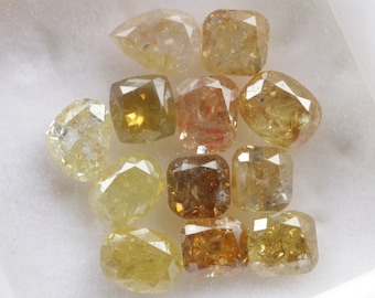 Puede incluir: Una colección de 12 diamantes en bruto de color amarillo, marrón y naranja. Los diamantes son de diversas formas y tamaños.