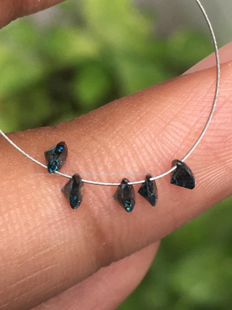 May include: A strand of dark blue faceted gemstone beads strung on a silver wire. The beads are triangular in shape and have a slight green hue.