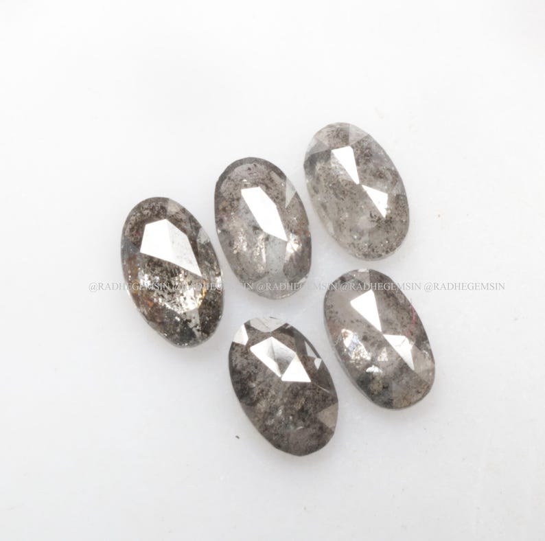 Pode incluir: Cinco diamantes cinzentos de forma oval com corte facetado. Os diamantes est&atilde;o dispostos em semic&iacute;rculo sobre uma superf&iacute;cie branca.
