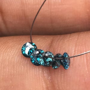 May include: A strand of blue round diamonds on a thin wire. The diamonds are faceted and have a teal blue color.