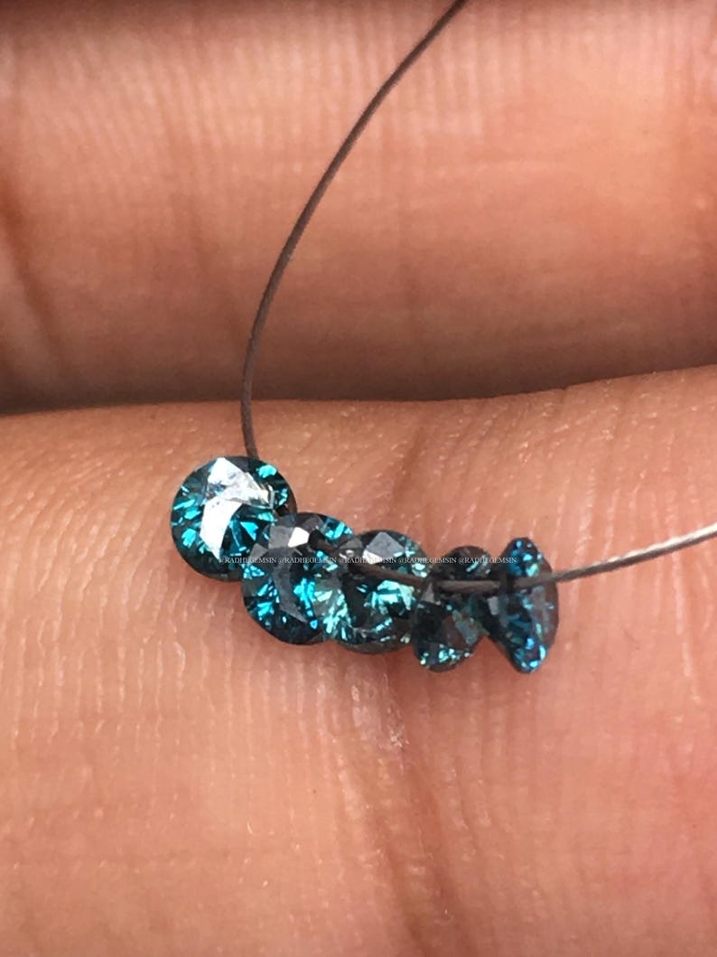 May include: A strand of blue round diamonds on a thin wire. The diamonds are faceted and have a teal blue color.