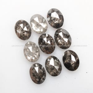 Pode incluir: Uma cole&ccedil;&atilde;o de dez diamantes brutos de corte oval, cinzentos e pretos. Os diamantes s&atilde;o de tamanhos diferentes e t&ecirc;m v&aacute;rias inclus&otilde;es.