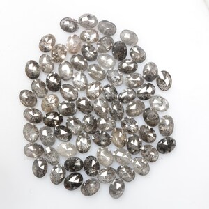 Pode incluir: Uma cole&ccedil;&atilde;o de diamantes cinzentos soltos, de forma oval, com um acabamento &aacute;spero e n&atilde;o cortado. Os diamantes est&atilde;o espalhados sobre uma superf&iacute;cie branca.