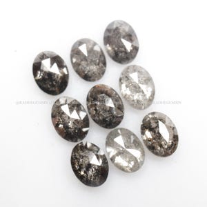 Pode incluir: Uma cole&ccedil;&atilde;o de nove diamantes negros de forma oval, com um corte bruto e facetado. Os diamantes t&ecirc;m um brilho prateado e est&atilde;o dispostos em uma pilha solta.