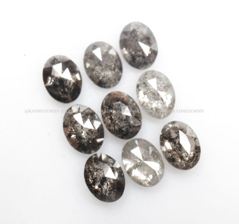 Pode incluir: Uma cole&ccedil;&atilde;o de nove diamantes negros de forma oval, com um corte bruto e facetado. Os diamantes t&ecirc;m um brilho prateado e est&atilde;o dispostos em uma pilha solta.