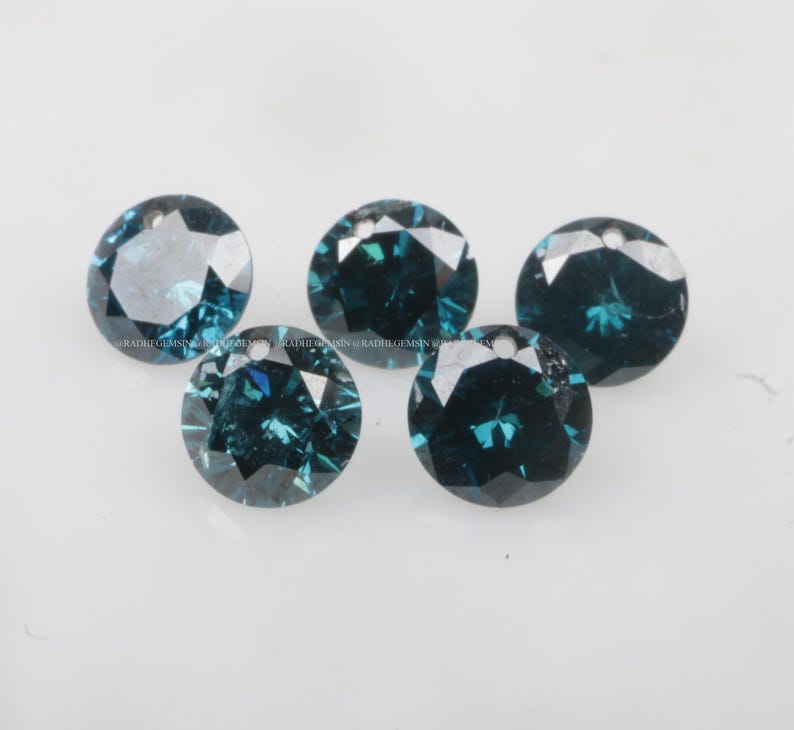 May include: Five round, teal blue gemstones with a faceted cut. The gemstones are arranged in a semi-circle on a white surface.