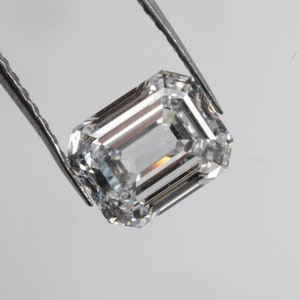 Pu&ograve; includere: Una gemma di diamante taglio smeraldo trasparente tenuta da una pinzetta.
