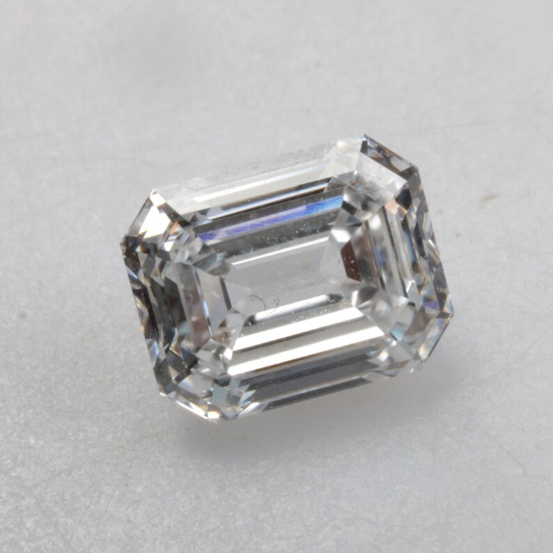 Pu&ograve; includere: Una pietra preziosa di diamante taglio smeraldo trasparente con sfaccettature.
