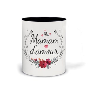 Peut inclure: Mug en céramique blanche avec un bord noir. Le mug présente une couronne florale noire et blanche avec le texte "Ma Maman d'amour" en lettres noires.