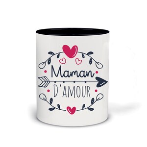 Op de afbeelding: Witte keramische mok met een zwarte rand. De mok heeft een zwart-witte illustratie van een hart met een pijl, bladeren en de tekst "Maman d'Amour".