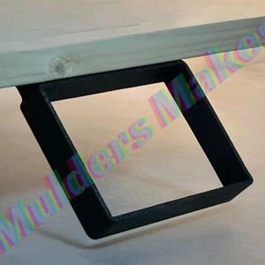 Może przedstawiać: Zbliżenie czarnego, kwadratowego wspornika nogi stołu przymocowanego do jasnej drewnianej powierzchni. Wspornik jest wykonany z metalu i ma minimalistyczny design, odpowiedni do różnych stylów mebli.