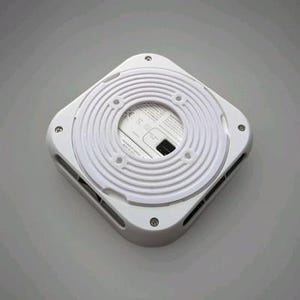 Puede incluir: Un dispositivo electrónico blanco de forma cuadrada con un diseño circular y estriado en el centro. El dispositivo tiene varios agujeros pequeños y rejillas de ventilación alrededor de los bordes y está asegurado con tornillos pequeños. Es probable que sea un producto para el hogar inteligente.