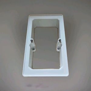 Può includere: Una scatola per prese elettriche rettangolare bianca con un design incassato. Due viti di montaggio sono visibili sui lati. La scatola è progettata per essere montata a parete.