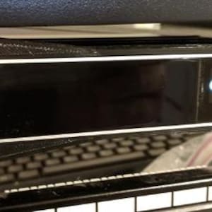 May include: A black electronic device with a white border is mounted on a rack. The device displays text on a small screen. Two silver bolts secure the device to the rack. The device is labeled "CLOUD KEY GEN2 PLUS".