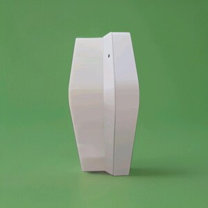 May include: A white, geometric object with a curved, symmetrical design. The object has a smooth, glossy finish and is set against a solid green background. The shape is reminiscent of a stylized vase or decorative piece.