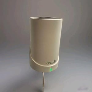 Könnte beinhalten: Ein zylindrisches, cremefarbenes Gerät mit gebogener Basis und flacher Oberseite. Der Text "deco 6e" ist auf der Seite aufgedruckt. Ein kleines grünes Licht leuchtet in der Nähe der Basis. Ein weißes Kabel erstreckt sich von unten.