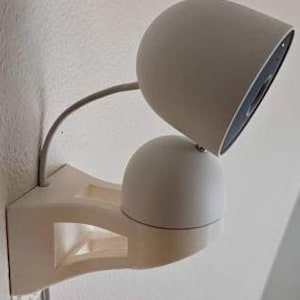 Puede incluir: Una lámpara de pared blanca y moderna con dos cabezales de luz redondeados y ajustables. La lámpara está fijada a un soporte geométrico blanco y tiene un brazo flexible gris. El diseño es minimalista y contemporáneo, adecuado para varios estilos de interior.