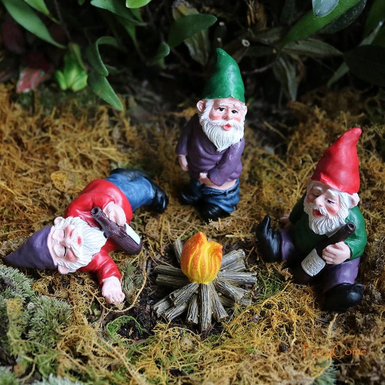 可能包括：三个迷你小矮人，一个躺着，一个站着，一个坐着，围坐在一个小篝火旁。小矮人们穿着色彩鲜艳的衣服和帽子，手里拿着瓶子。