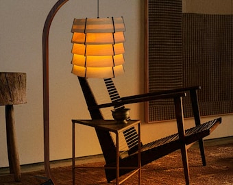 May include: A wooden floor lamp with a tiered, layered lampshade. The lamp has a curved, dark brown wooden frame. The lampshade emits a warm, yellow light. The lamp is in a room with a wooden chair and a small side table.