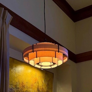 Puede incluir: Una l&aacute;mpara colgante circular de estilo moderno de mediados de siglo. La luz tiene un brillo naranja c&aacute;lido y est&aacute; suspendida del techo. La habitaci&oacute;n cuenta con una chimenea, obras de arte y un sof&aacute;.