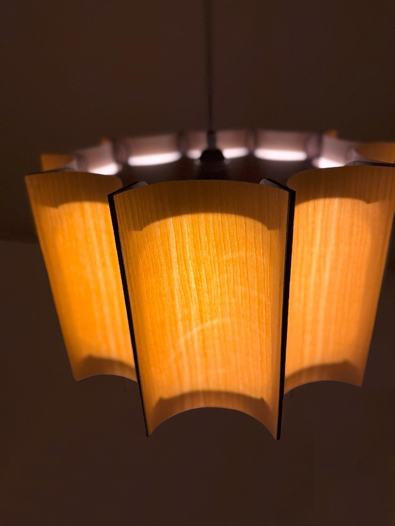 May include: A mid-century modern pendant light fixture with a warm, inviting glow. The light has a wooden shade with a curved design and a dark trim. The light is suspended from the ceiling by a thin wire.