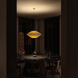 May include: A modern dining room featuring a round table set for a meal. A geometric, layered pendant light fixture hangs above the table. The room is dimly lit, with dark chairs and a neutral color palette.