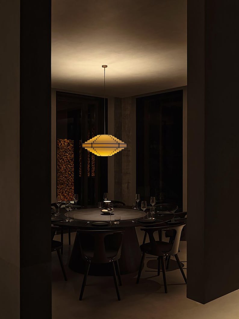 May include: A modern dining room featuring a round table set for a meal. A geometric, layered pendant light fixture hangs above the table. The room is dimly lit, with dark chairs and a neutral color palette.