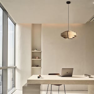 Puede incluir: Oficina moderna con l&aacute;mpara colgante de madera. Un escritorio con port&aacute;til y silla se encuentra cerca de una gran ventana. El espacio es minimalista, con tonos neutros y peque&ntilde;as estanter&iacute;as en la pared.
