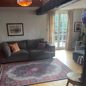 Puede incluir: Un sal&oacute;n con un sof&aacute; gris, una alfombra estampada y suelo de madera. La alfombra tiene un dise&ntilde;o rojo y azul. Una peque&ntilde;a mesa roja se encuentra junto al sof&aacute;. Una l&aacute;mpara decorativa cuelga del techo.