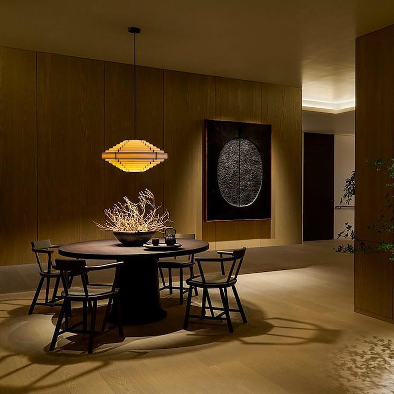 May include: A modern dining room with a round wooden table and six black chairs. A decorative light fixture hangs above the table. A large piece of art hangs on the wall. The room has a warm, inviting atmosphere.