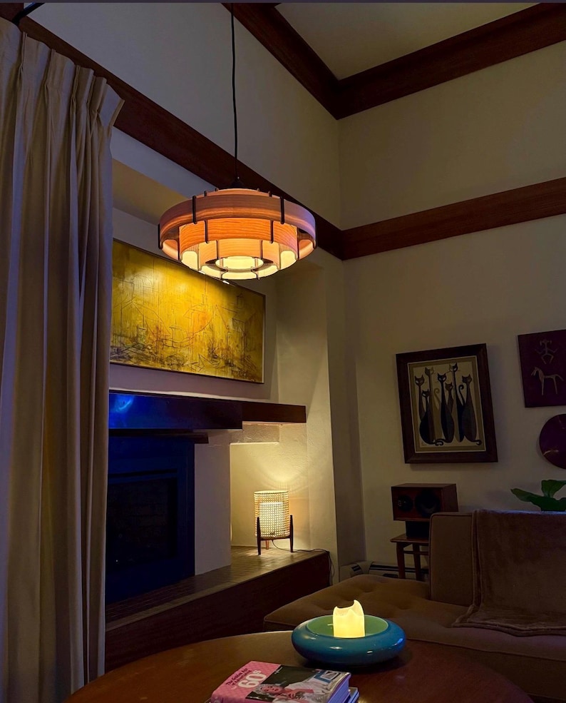 Puede incluir: Una l&aacute;mpara colgante circular de estilo moderno de mediados de siglo. La luz tiene un brillo naranja c&aacute;lido y est&aacute; suspendida del techo. La habitaci&oacute;n cuenta con una chimenea, obras de arte y un sof&aacute;.