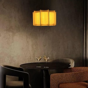 May include: A modern interior scene featuring a rectangular, illuminated light fixture with a warm, yellow glow. Below, a dark round table is set with two martini glasses. The scene includes dark chairs with unique designs, creating a sophisticated ambiance.